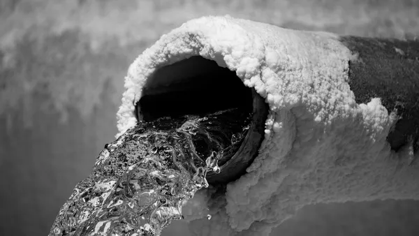 Water gushing from a pipe whose rim is coated in whitish crystalline build-up, black-and-white photograph