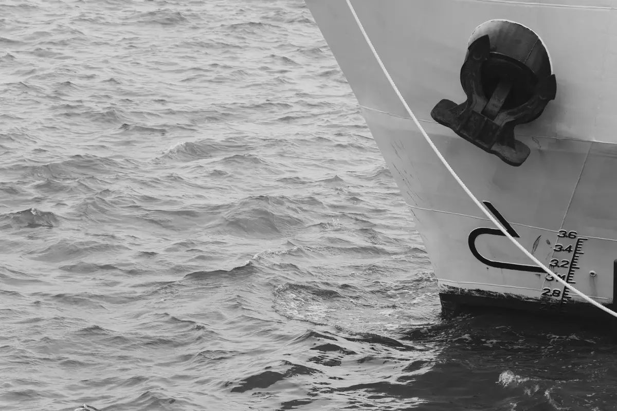 Bow of a ship with the anchor stowed in its hawse hole and a diving depth scale painted on the hull, rippled sea, black-and-white photograph