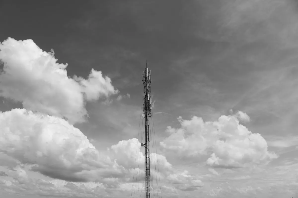 Traliccio di un’antenna per telecomunicazioni contro un cielo nuvoloso, in bianco e nero