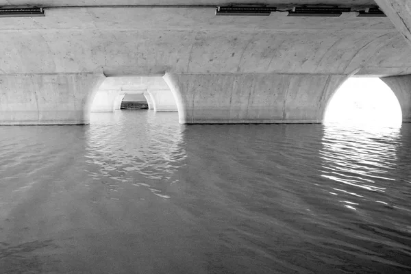 Arcate in calcestruzzo di un attraversamento viste dal pelo dell’acqua, in bianco e nero