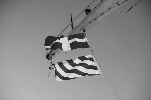 Two maritime signal flags hoisted on a yardarm against the sky