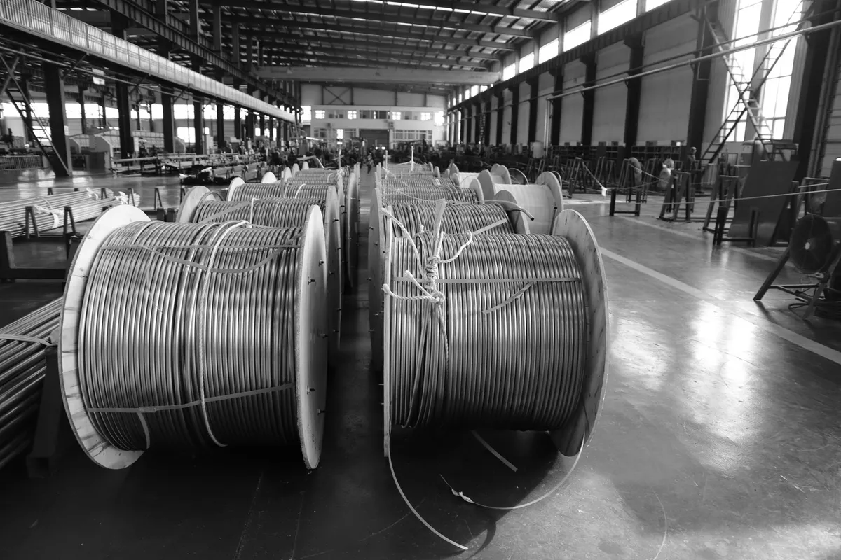 File di bobine avvolte di cavo in un capannone industriale, in bianco e nero