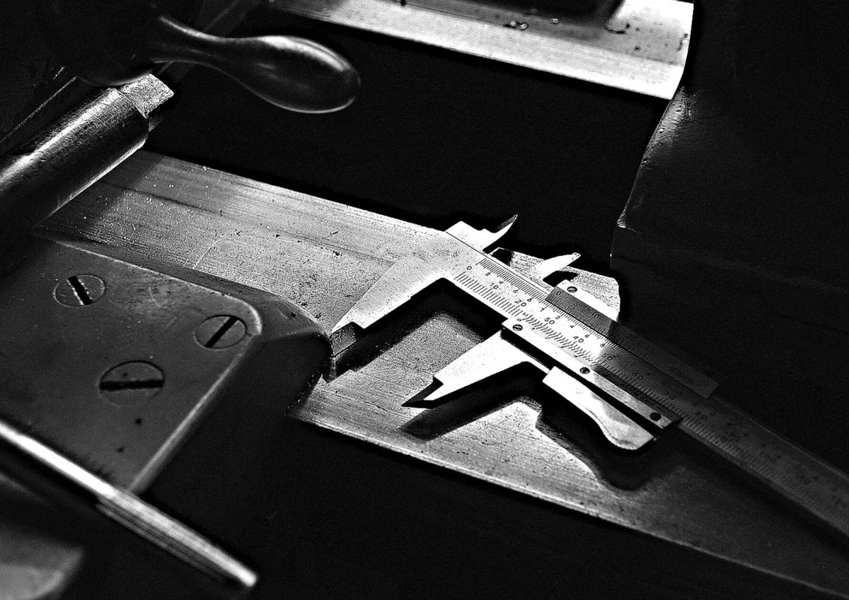 Calibro a corsoio metallico appoggiato su un pezzo lavorato, in un’officina in penombra, fotografia in bianco e nero