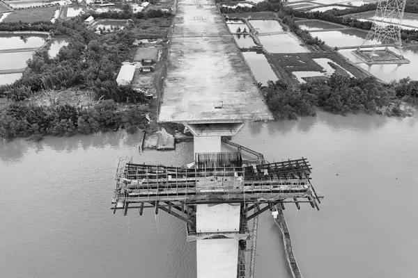The deck of a bridge under construction stopping in mid-air above the water, with the next pier still in falsework