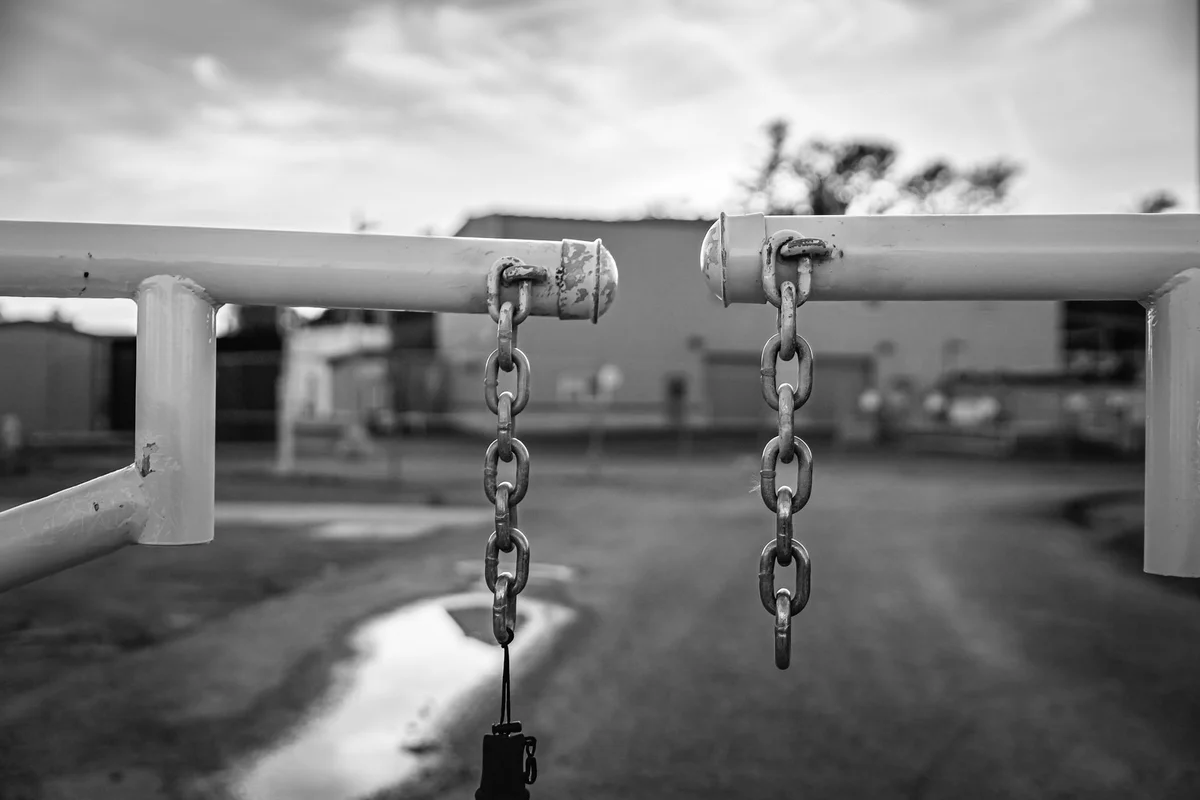 Due bracci di una sbarra industriale con catene di chiusura appese, in bianco e nero