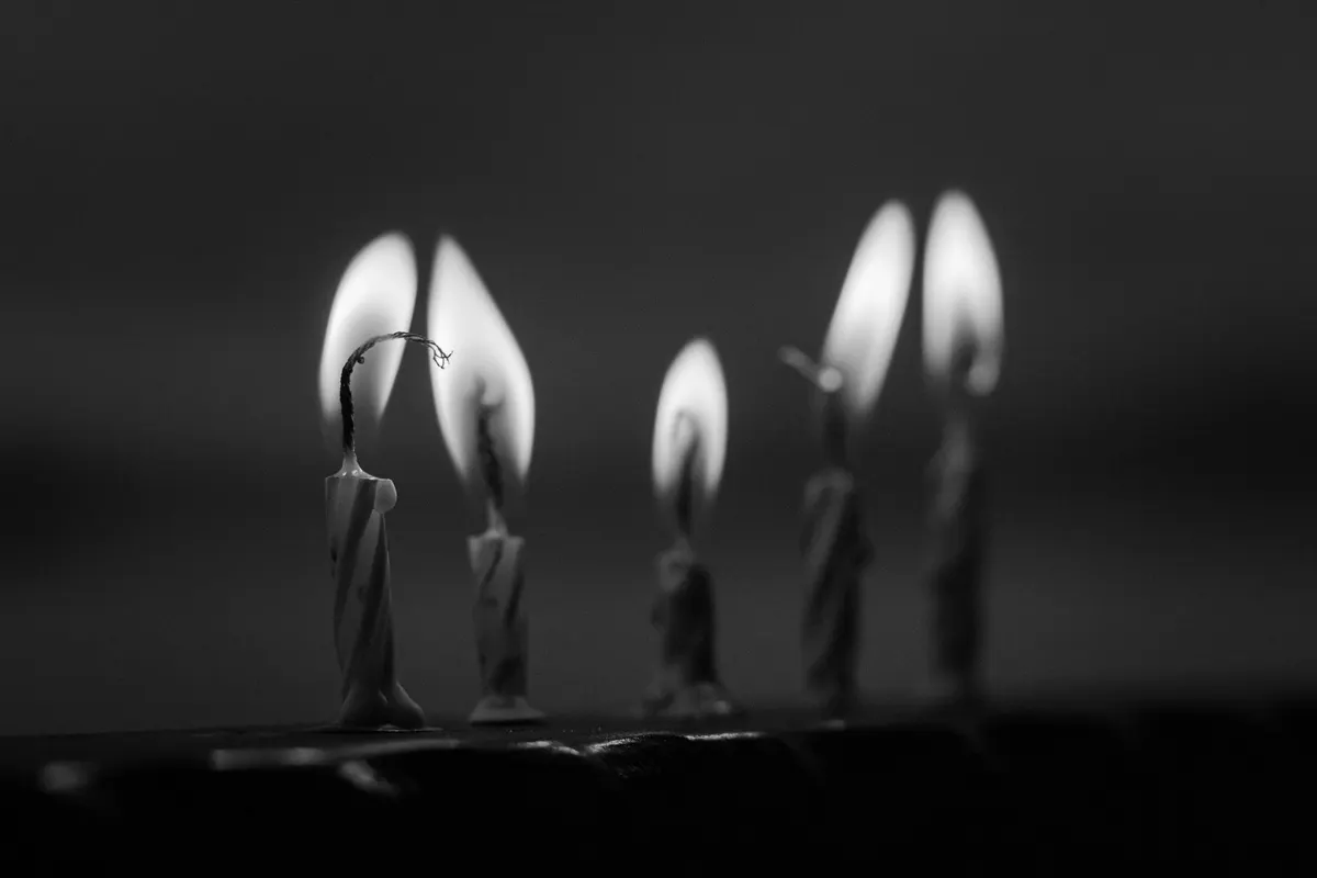Cinque candeline accese, consumate a lunghezze diverse, allineate su un bordo scuro, fotografia in bianco e nero