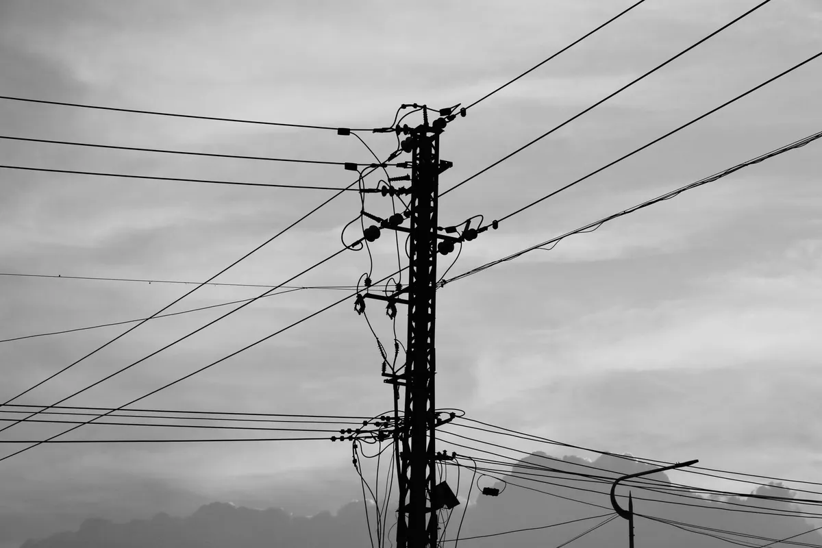 Lattice pole with insulators and several bundles of aerial cables at different heights, backlit, in black and white