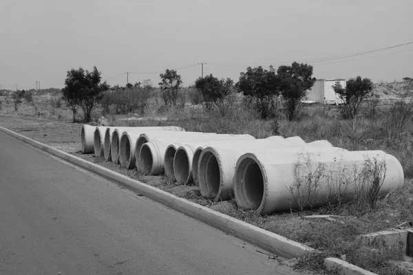 Row of large empty concrete pipes stacked at the roadside, black-and-white photograph
