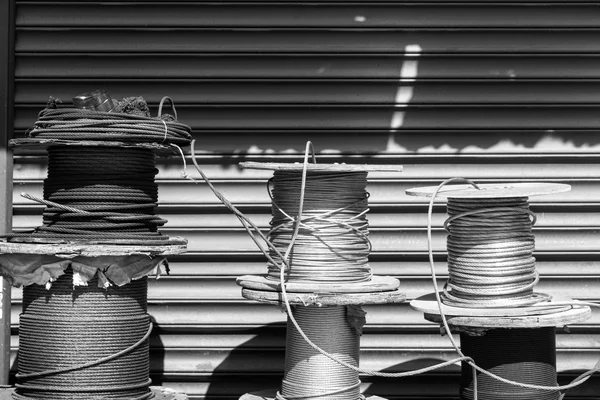 Three coils of braided metal cable of different thicknesses, standing in front of a roller shutter, black and white