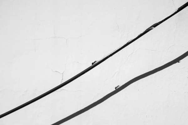 Black cable running diagonally across a cracked plastered wall, in black and white