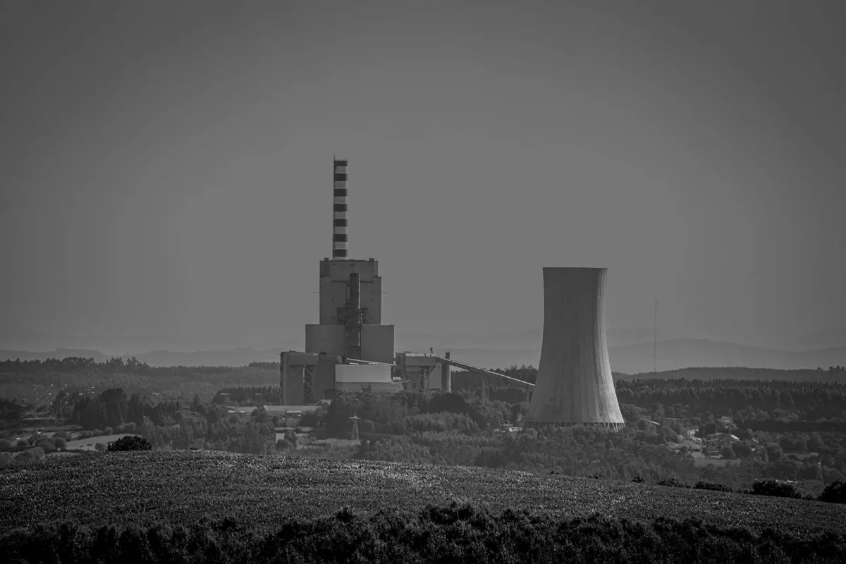 Ciminiera e torre di raffreddamento di una centrale elettrica dismessa, in bianco e nero, su un paesaggio di campagna