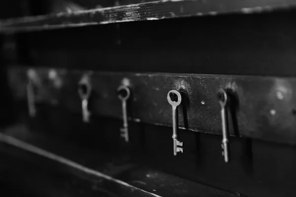 A bunch of old metal keys hanging on hooks against a dark wooden board, black-and-white photograph