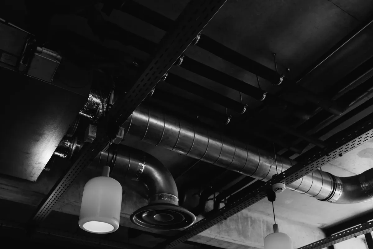 Metal ventilation ducts on a ceiling with joints and a round diffuser, black and white photograph