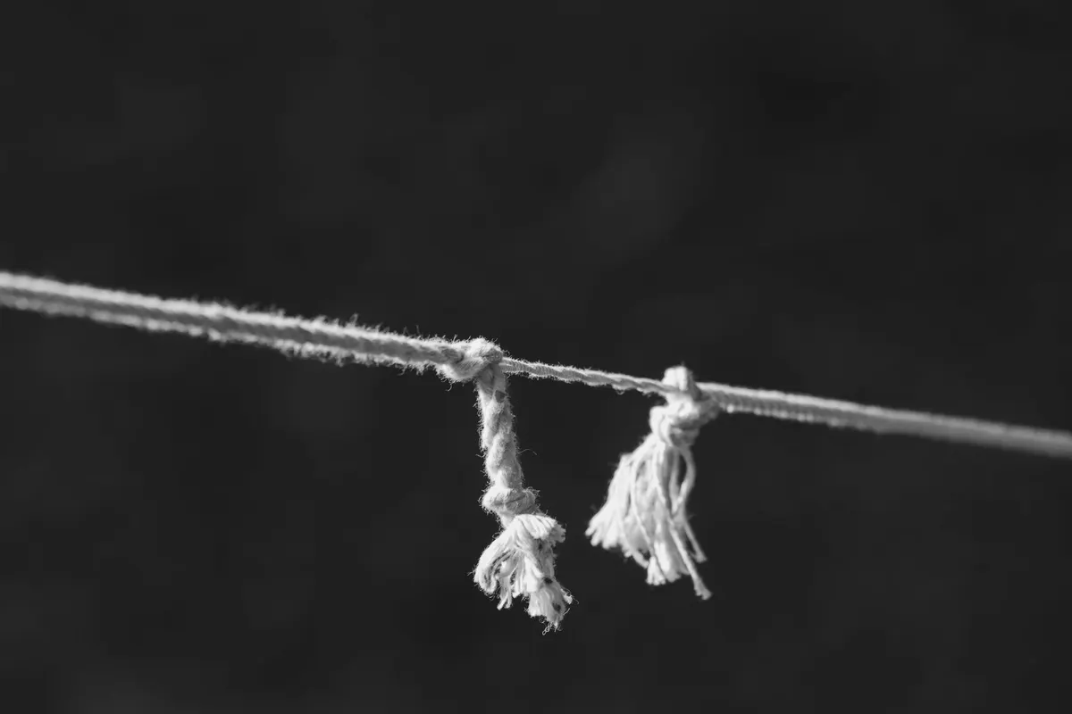 A rope knotted midway along a taut line, with two frayed ends hanging loose, black and white photograph
