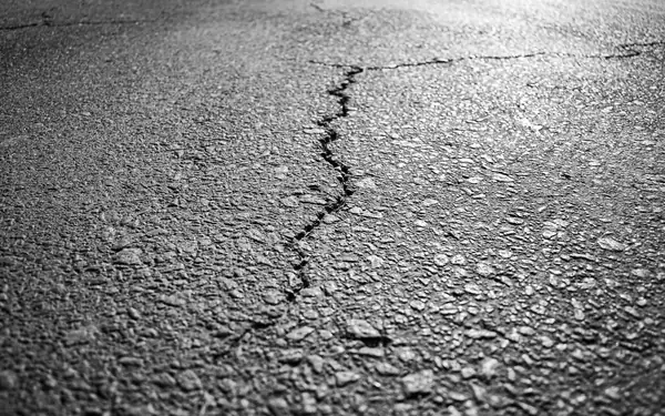 Crack running across an asphalt road surface, close-up detail, black-and-white photograph