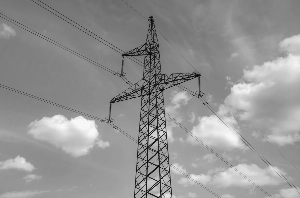 Traliccio dell’alta tensione visto dal basso contro un cielo azzurro con nuvole