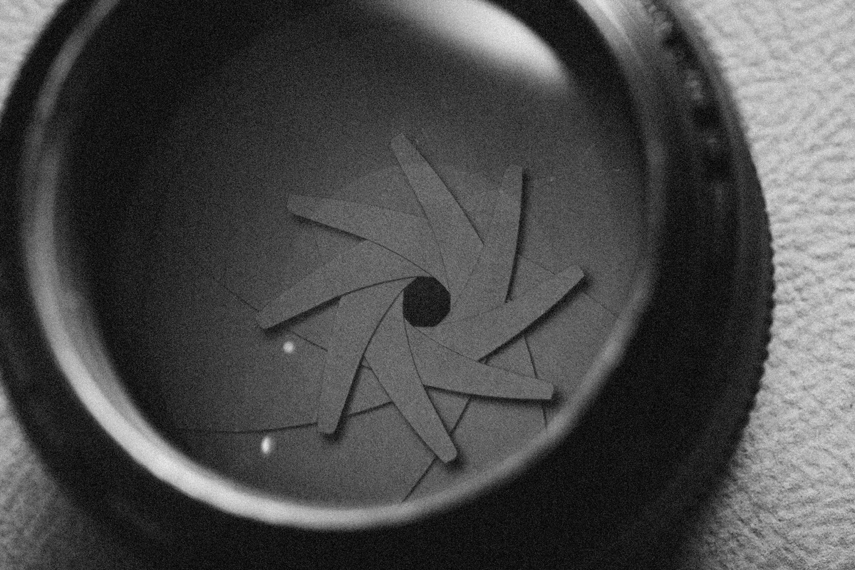 Close-up macro of a camera lens iris diaphragm, almost closed, in black and white