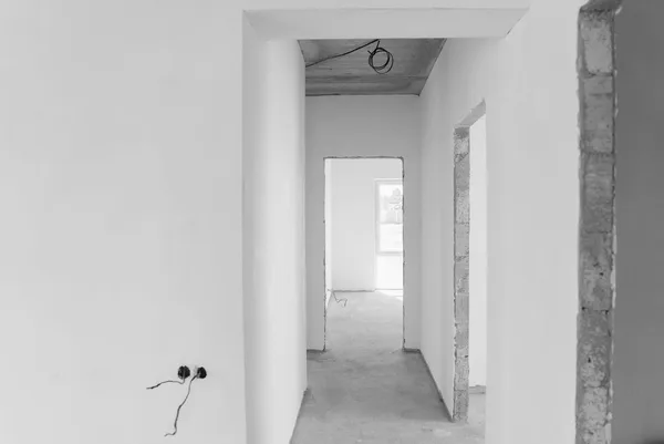 Corridoio di un edificio al grezzo con pareti intonacate, pavimento in cemento e una scatola elettrica con i fili ancora scoperti