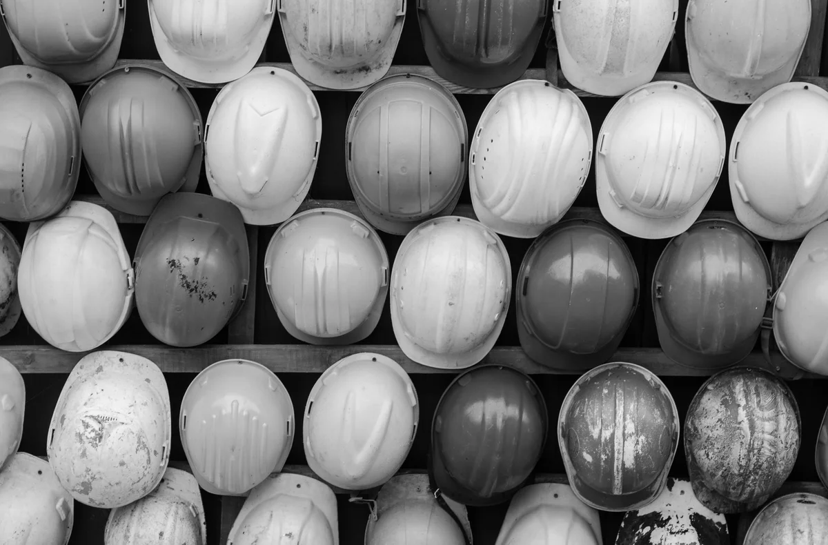 Fila di caschi da cantiere di colori diversi appesi a una rastrelliera di legno, fotografia in bianco e nero