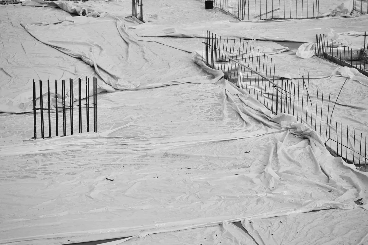 Ferri di armatura che sporgono da un getto di fondazione coperto con un telo di polietilene, in bianco e nero