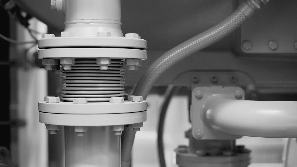 Flangia bullonata con giunto a soffietto su una tubazione industriale, ripresa da vicino, in bianco e nero