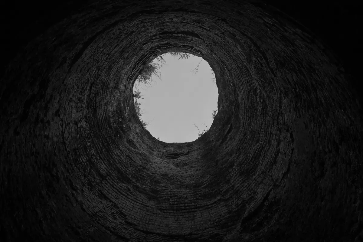 View from the bottom of a well looking up towards the opening, brick walls in concentric rings, black and white photograph