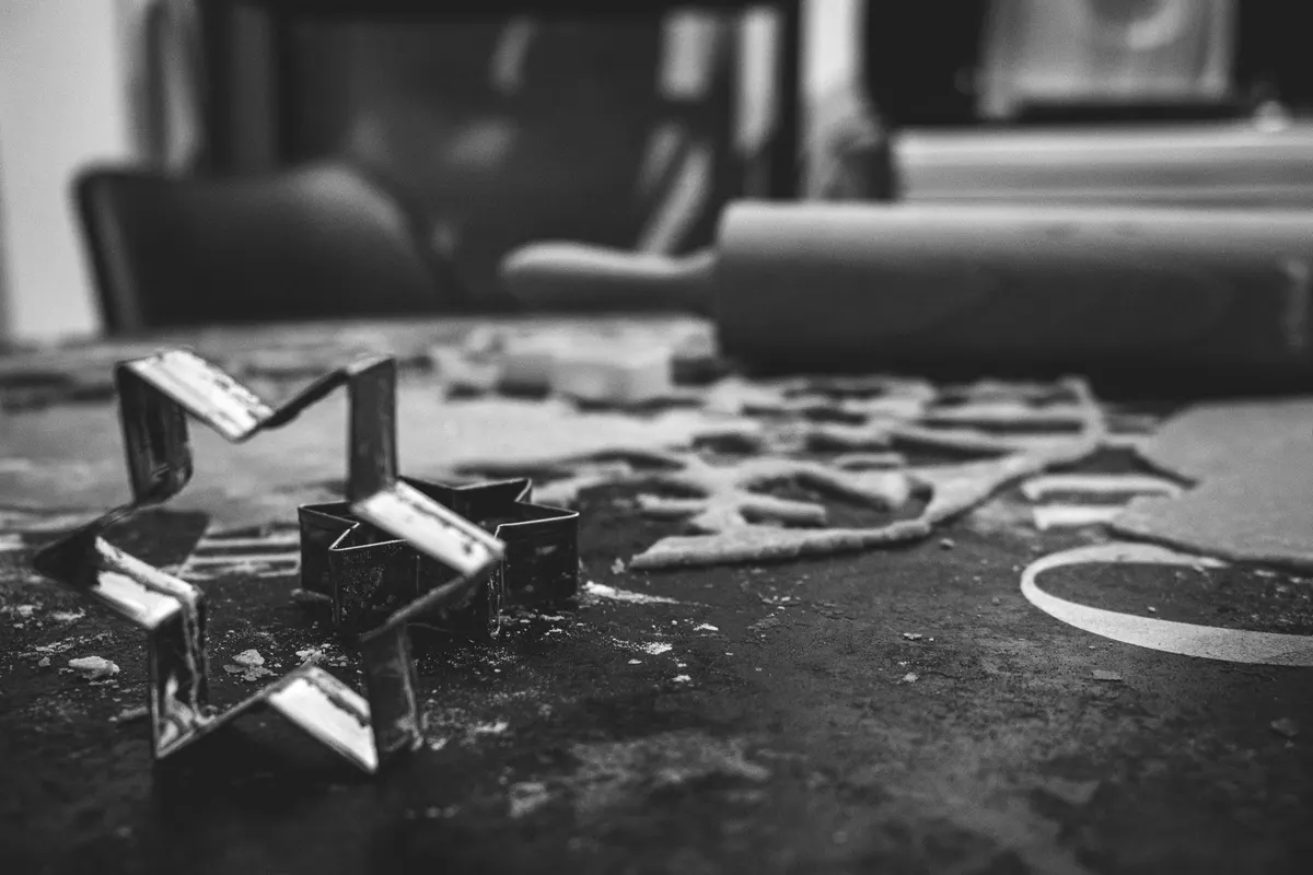 Star-shaped metal cookie cutters on a floured work surface, behind them the rolled sheet with the shapes already cut out and a rolling pin, black and white photograph