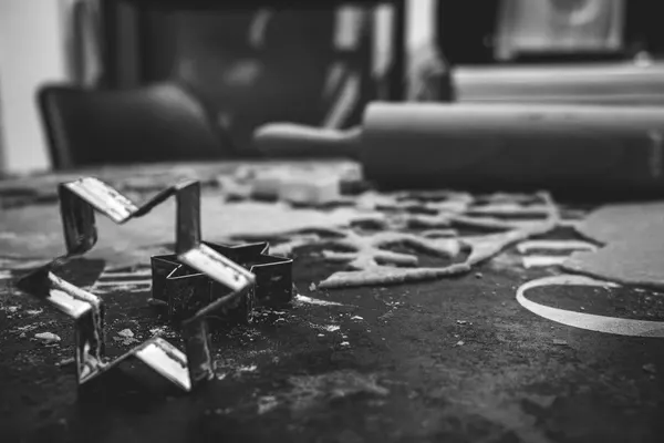 Star-shaped metal cookie cutters on a floured work surface, behind them the rolled sheet with the shapes already cut out and a rolling pin, black and white photograph