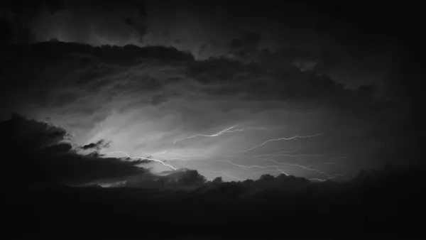 Branching lightning bolts crossing a night sky heavy with storm clouds, black and white photograph