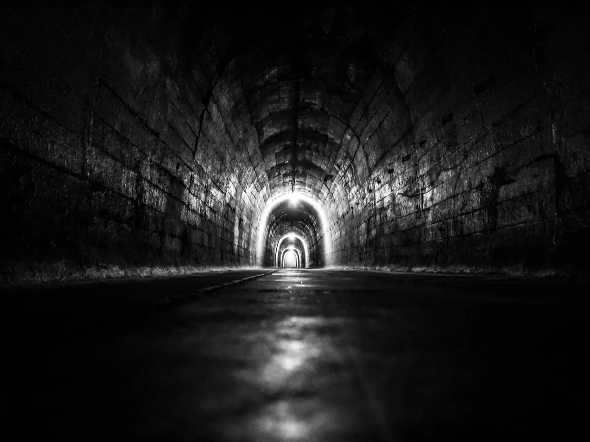 Galleria interrata a volta in muratura, illuminata da punti luce lungo il percorso, fotografia in bianco e nero
