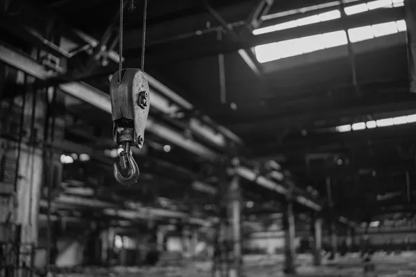 Hook and pulley block of a hoist hanging from the ceiling of a disused industrial warehouse, black-and-white photograph