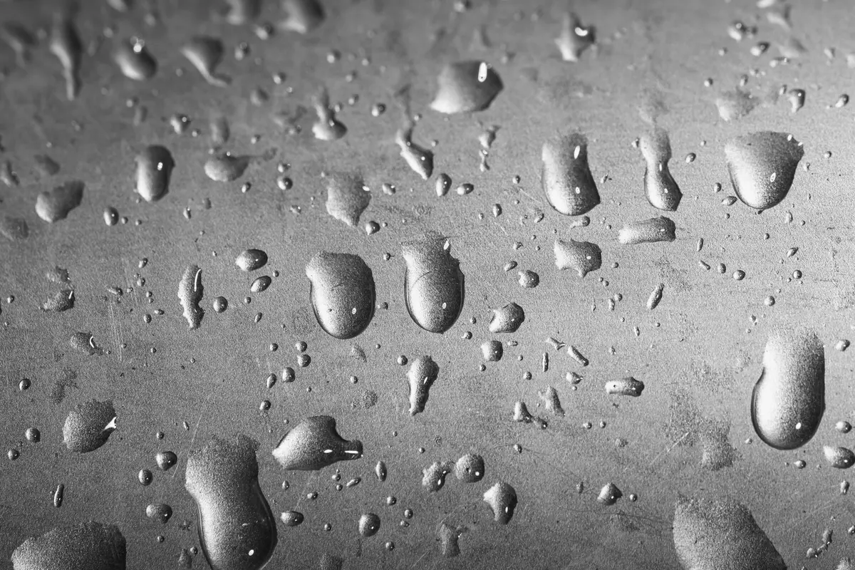 Gocce d’acqua su una superficie metallica graffiata, macrofotografia in bianco e nero