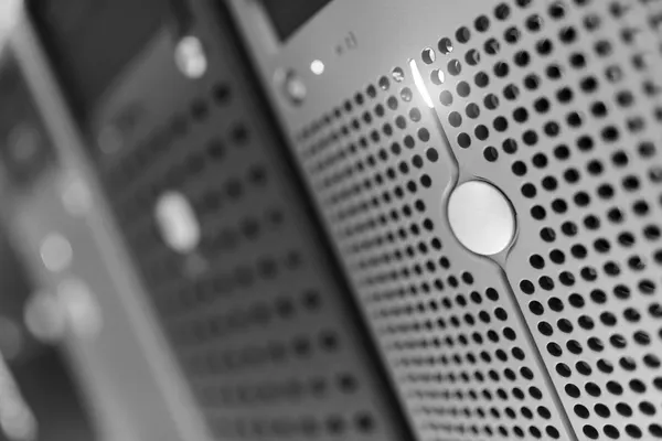 Perforated front panel of a rack-mounted server seen at an angle, with other blurred equipment panels in the background, black and white photograph