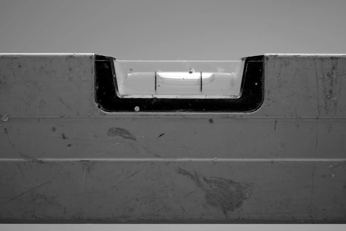 Primo piano della fiala di una livella a bolla incassata in un corpo metallico graffiato, la bolla sconfina oltre la tacca di destra, fotografia in bianco e nero