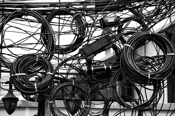 A tangle of aerial cables coiled in loops with splice closures hanging among them, black-and-white photograph