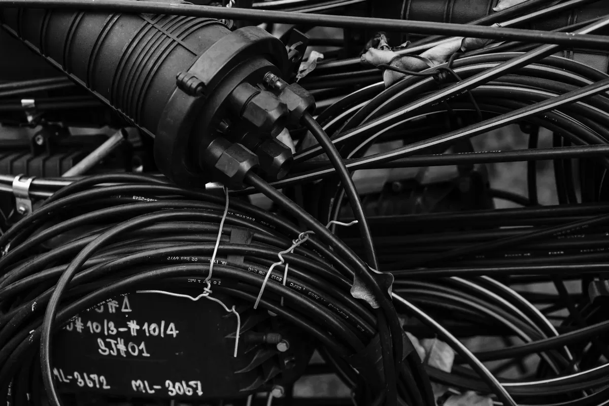 An aerial splice closure with coils of optical cable and hand-written route tags, in black and white