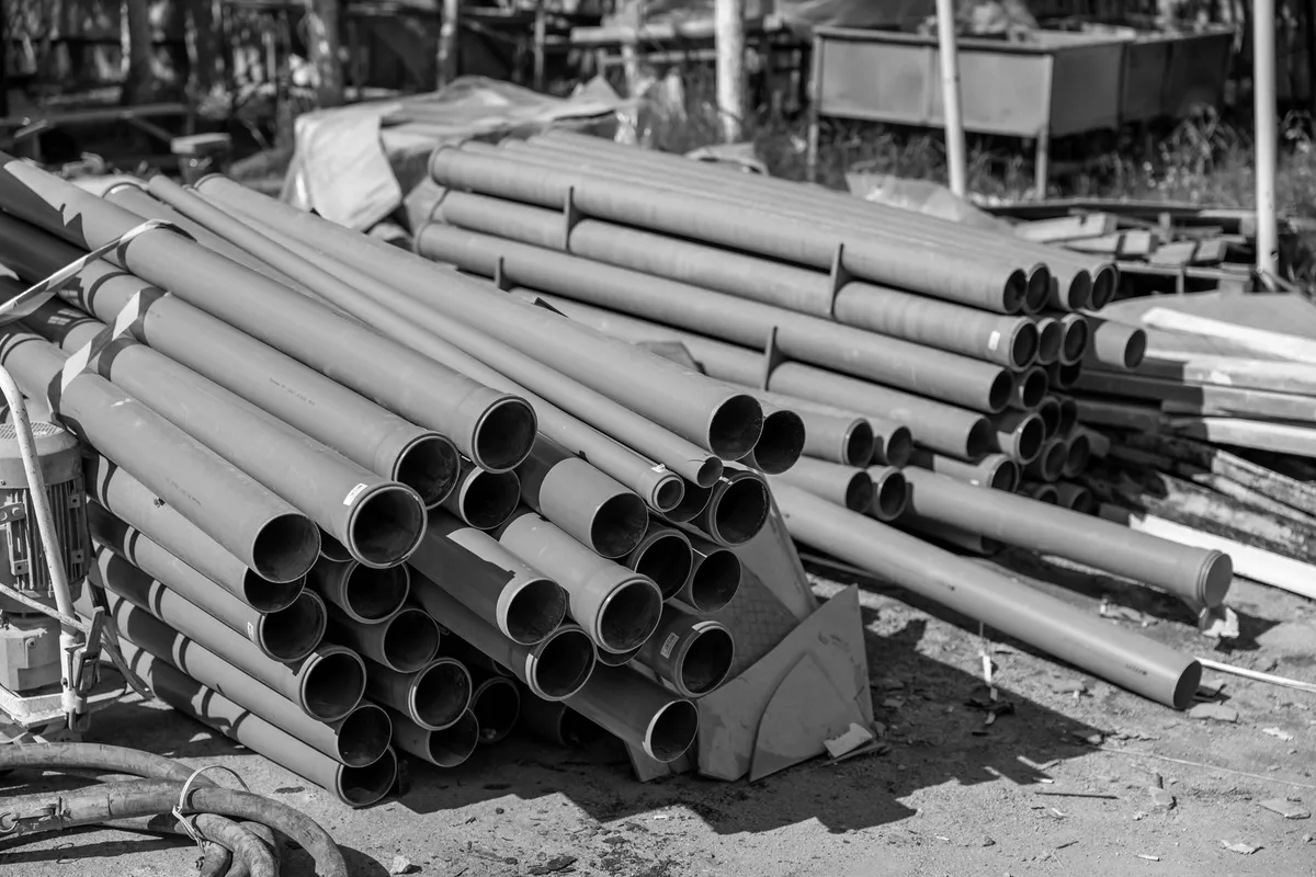 Small-diameter grey PVC pipes stacked on a construction site, in black and white