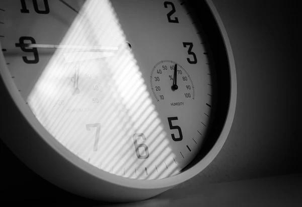 Close-up of a wall clock with a diagonal beam of light across the dial, in black and white