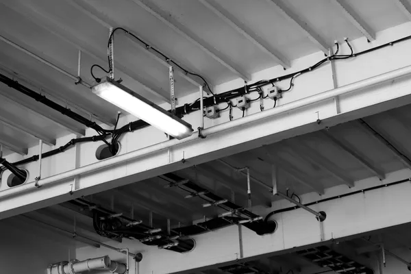 Bundles of cables passing through circular openings in a metal bulkhead, with cable trays, conduits and junction boxes, black and white photograph