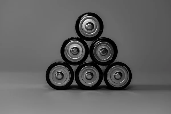 Six cylindrical cells stacked in a pyramid, seen from the positive terminal, black-and-white photograph on a neutral grey background