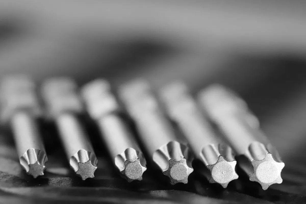 Sei punte di precisione in acciaio allineate in fila, riprese in macro, con le estremità sfalsate, in bianco e nero