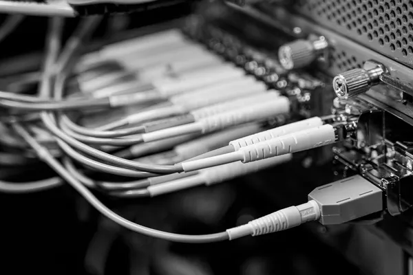 A bundle of fibre patch cords converging on the ports of a card in a chassis, with two knurled thumbscrews on the right, close-up black-and-white detail