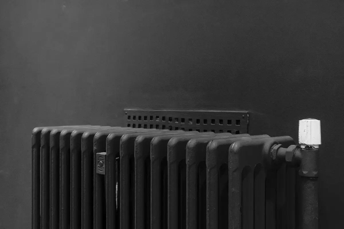 Cast-iron column radiator with a valve and a pale handwheel against a plain wall, black and white photograph