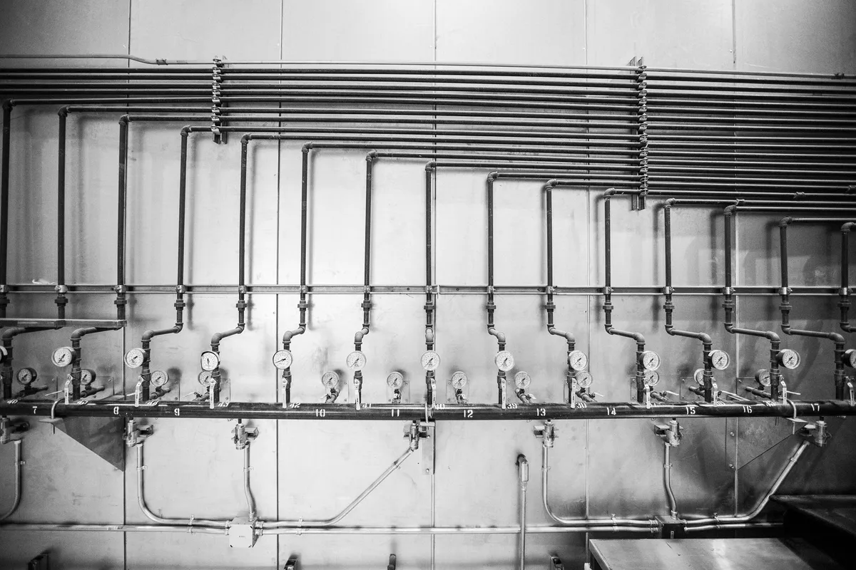 Fila di manometri e valvole numerate su un collettore industriale, in bianco e nero
