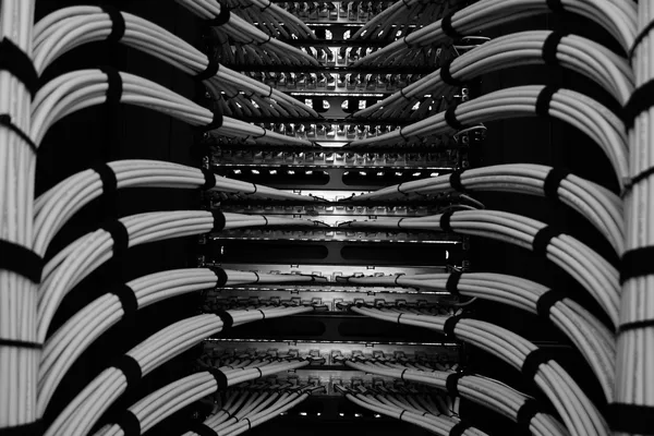 Retro di un armadio di permutazione con fasci ordinati di cavi che scendono verso i pannelli, in bianco e nero