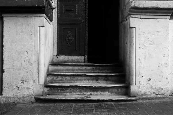 Worn stone steps in front of a door opening onto a dark interior
