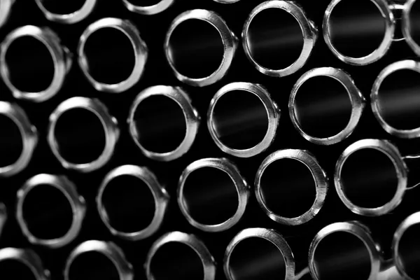 A bundle of round metal tubes seen end-on, stacked and slightly staggered, in black and white