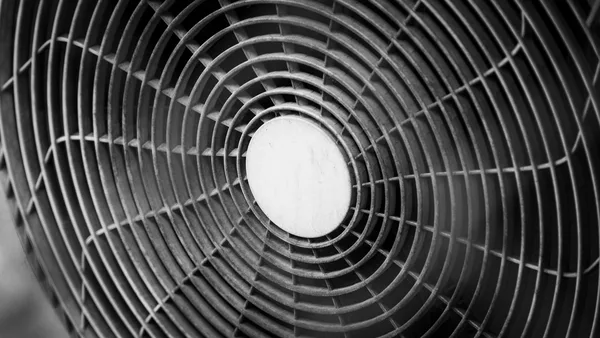 Close-up of the circular grille of an industrial fan, concentric rings and metal spokes, a smooth white hub at the centre, black and white photograph